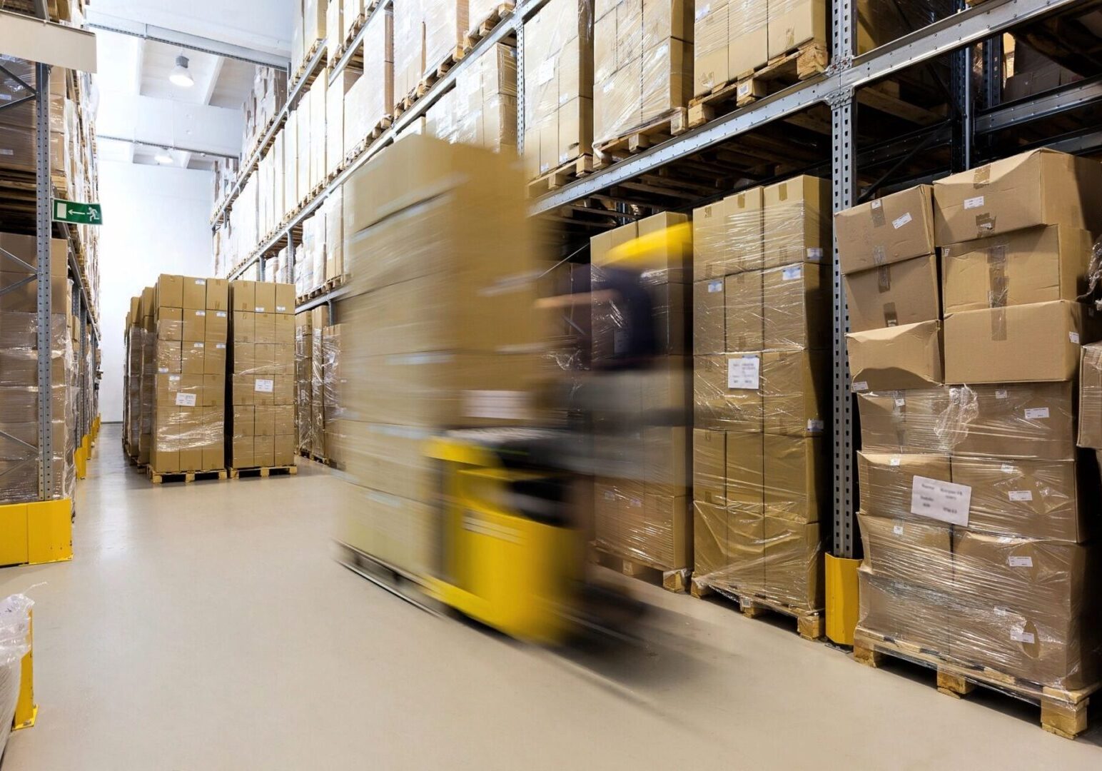 A yellow forklift moving through an aisle in a warehouse.